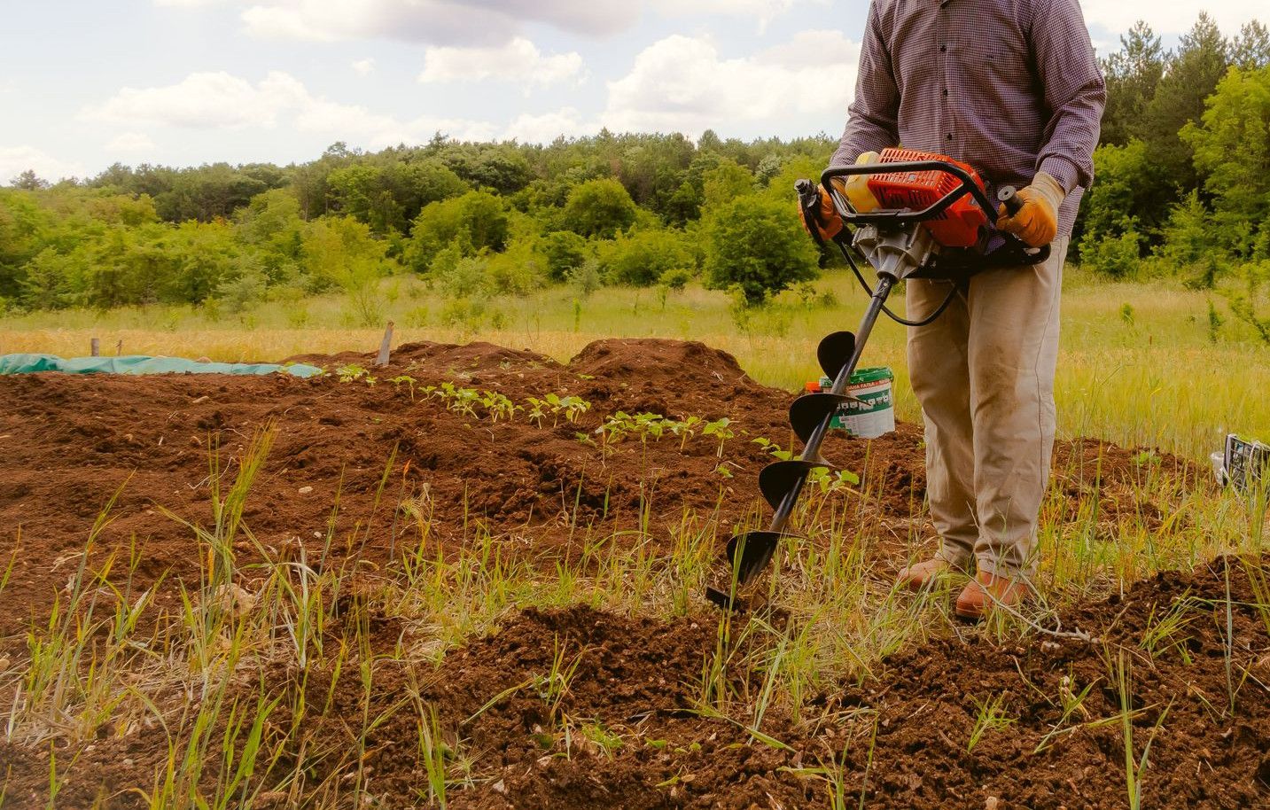 A farmer operates an earth auger in a lush field under a cloudy sky in Vize, Türkiye.